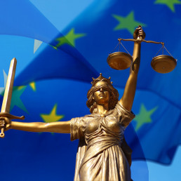 Goldene Statue der Göttin Justitia vor EU-Flagge.